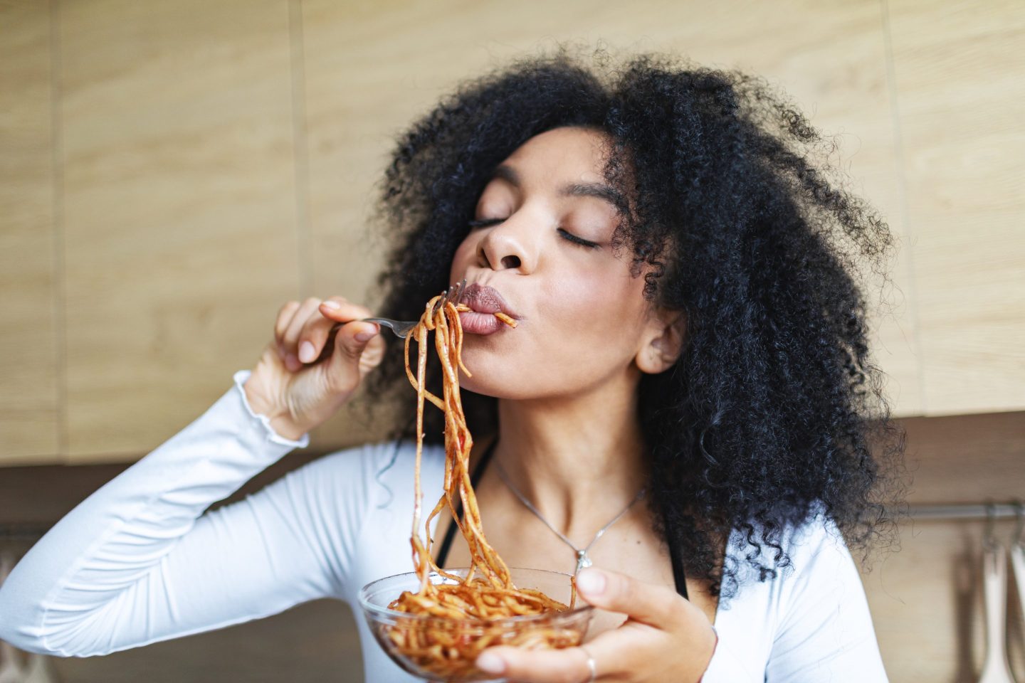 Young adult woman eating spaghetti at the kitchen